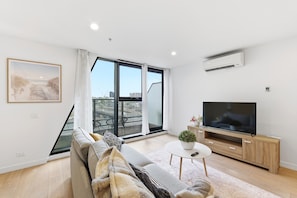 Ein modernes Wohnzimmer mit einer Couch, einem Fernseher und einem Balkon mit Blick auf die Stadt.