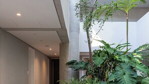 A modern indoor space with a concrete planter with plants, a tiled floor, and a hallway leading to another room. - Casa Omaguás by Viva | Apartamentos modernos no coração de Pinheiros (São Paulo)