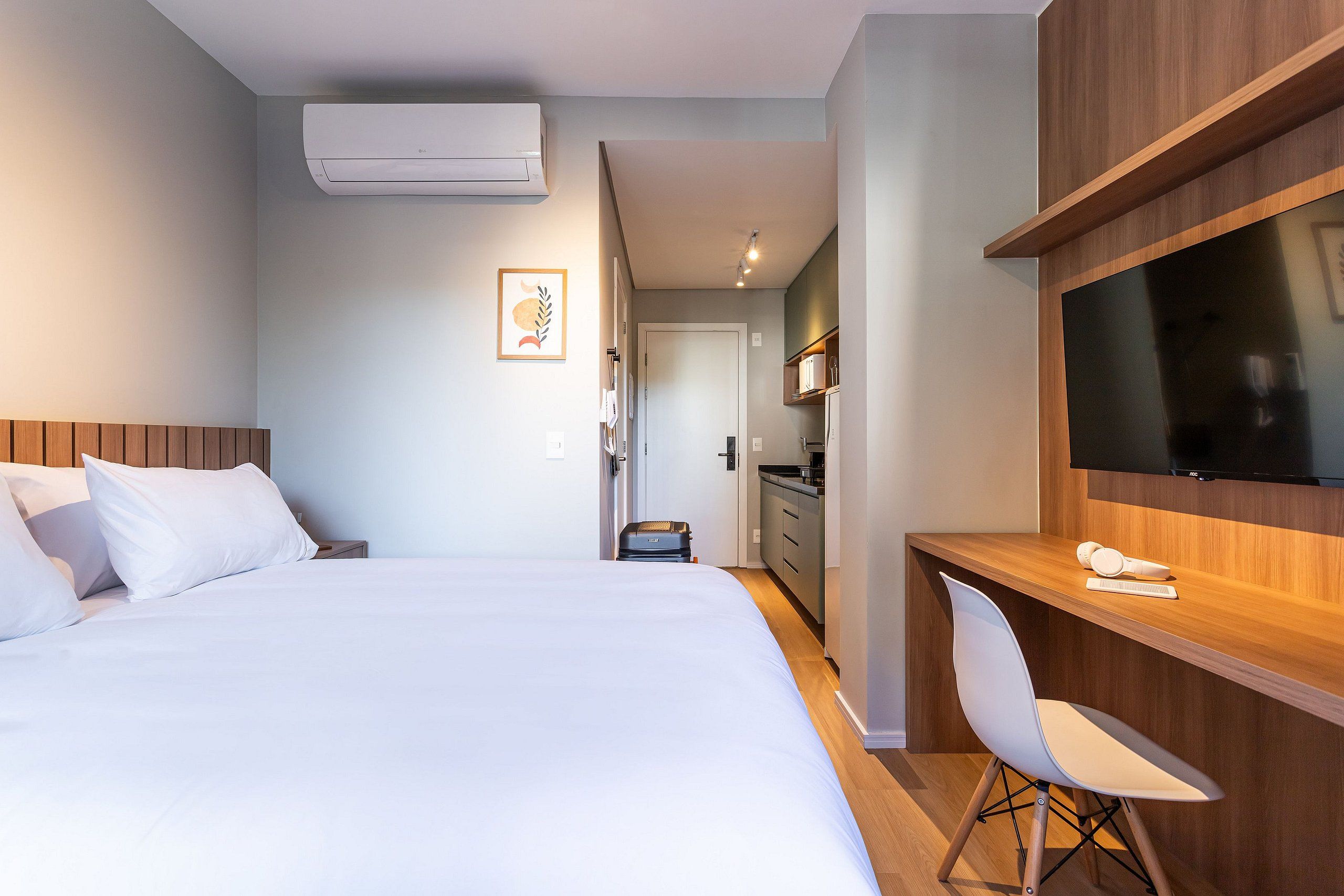 A hotel room with a bed, a desk, a chair, a TV, and a kitchenette.