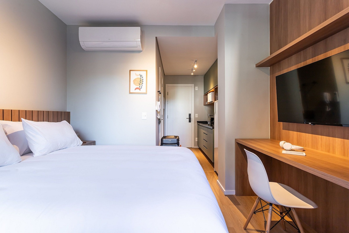 Una habitación de hotel con una cama, un escritorio, una silla, un televisor y una kitchenette.