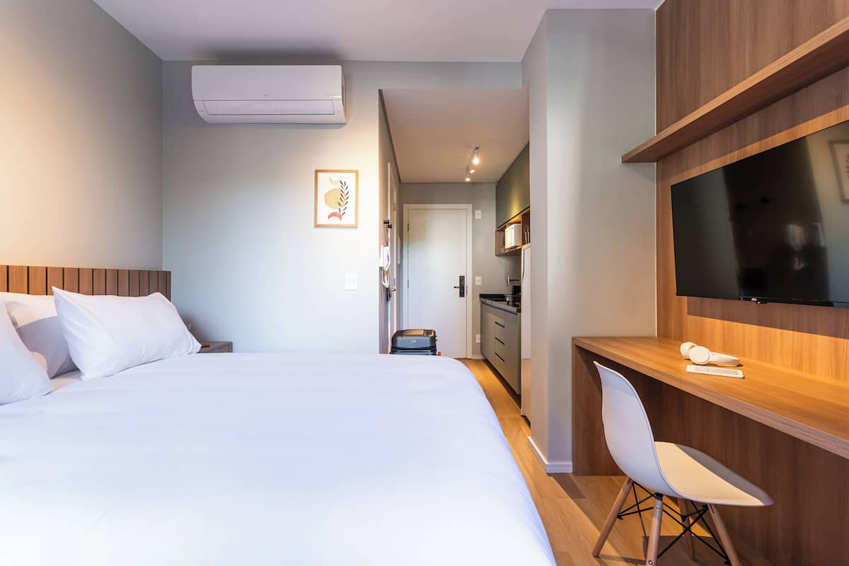 Una habitación de hotel con cama, escritorio, silla, televisión y kitchenette.