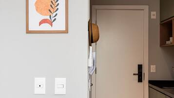 Une pièce comprenant un lit, une porte, un luminaire fixé au mur, un tableau encadré et un panier en osier.