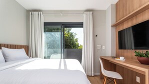 A modern hotel room with a large bed, a desk, a chair, a TV, and a balcony with curtains. - Casa Omaguás by Viva | Apartamentos modernos no coração de Pinheiros (São Paulo)