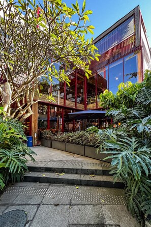 Un edificio moderno con fachada de vidrio, zona de estar exterior y una escalera que lleva a la entrada.