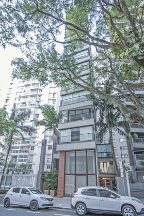 Un edificio de varios pisos con balcones, ventanas amplias y un automóvil blanco estacionado frente a él.