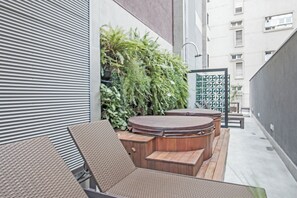 A modern outdoor seating area with a hot tub, surrounded by greenery and a metal gate. - Casa Omaguás by Viva | Apartamentos modernos no coração de Pinheiros (São Paulo)