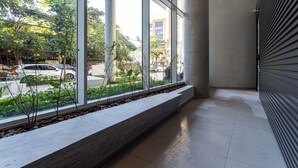 A corridor with large windows, a tiled floor, and a planter with plants. - Casa Omaguás by Viva | Apartamentos modernos no coração de Pinheiros (São Paulo)