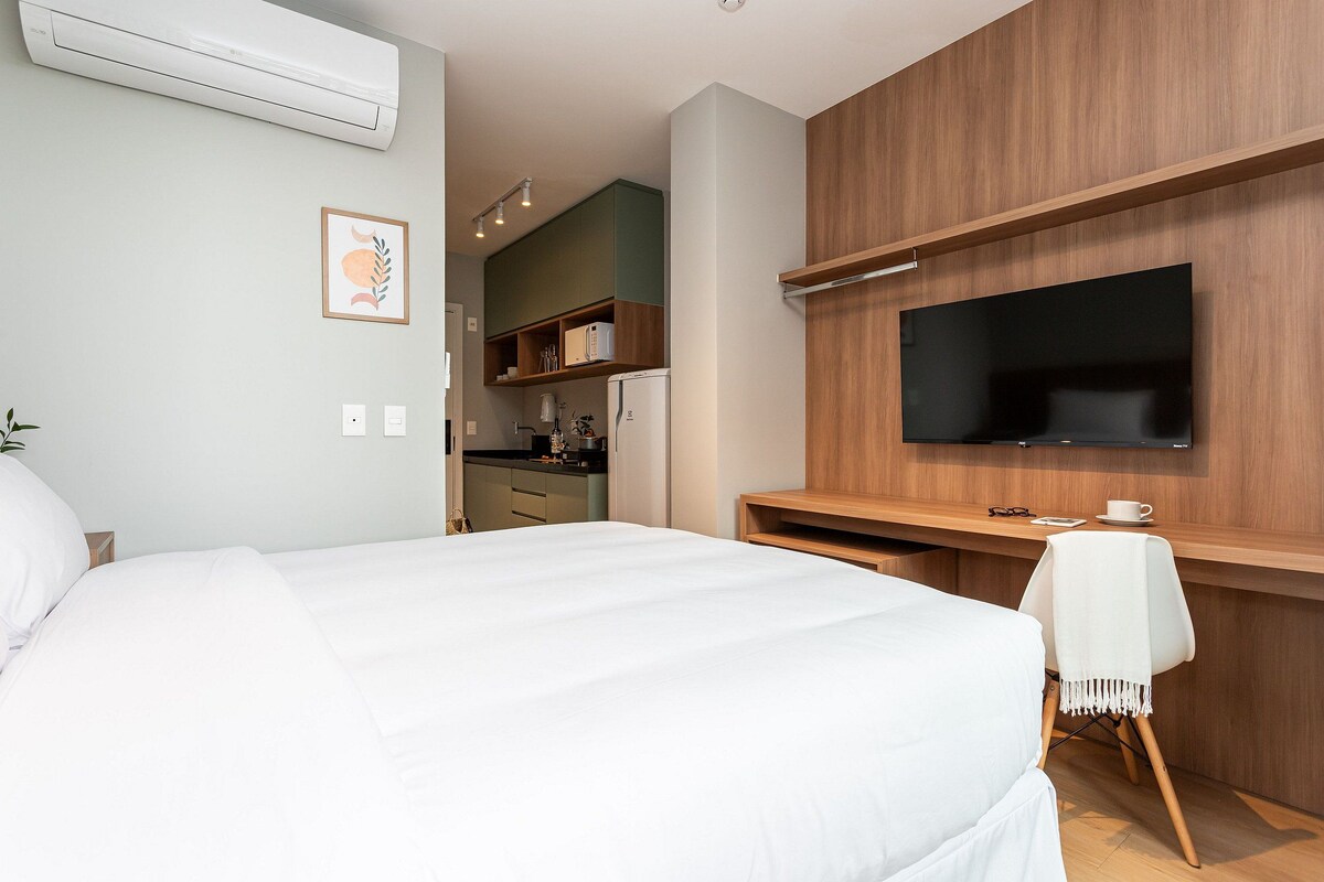 Una habitación de hotel con una cama, un escritorio con televisor, una kitchenette y un equipo de aire acondicionado.