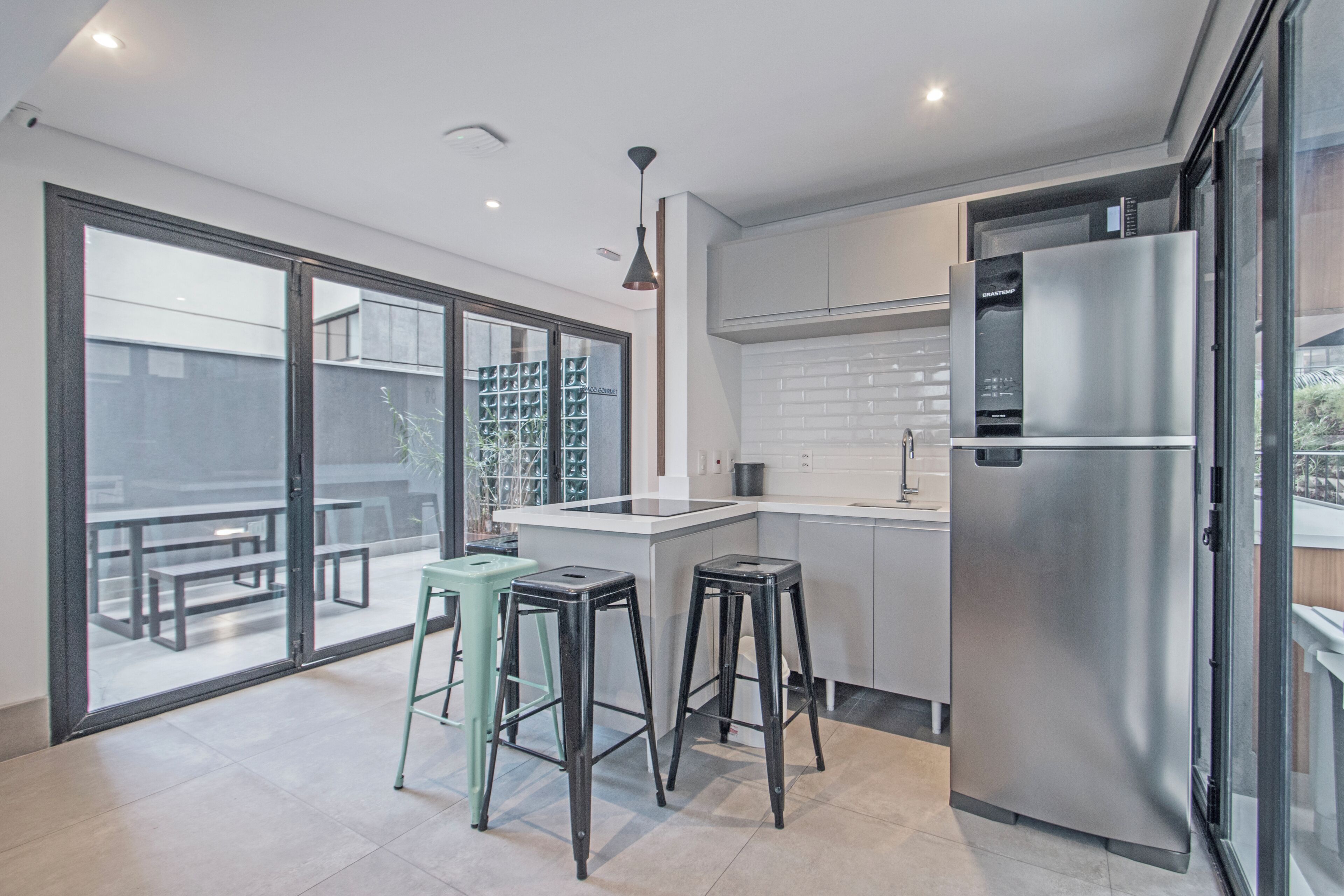 Una cocina moderna con un refrigerador de acero inoxidable, un comedor con taburetes y un amplio ventanal corredera que da a un patio exterior.