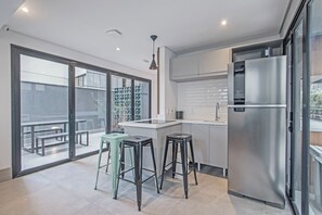 Una cocina moderna con un refrigerador de acero inoxidable, un comedor con taburetes y un amplio ventanal corredera que da a un patio exterior.