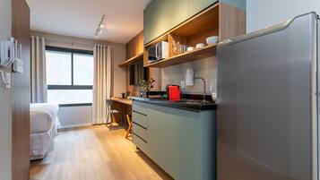 A compact kitchen with a built-in microwave, a coffee machine, and a refrigerator.
