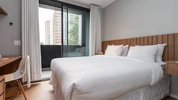 Une chambre d’hôtel avec un grand lit, un bureau, une chaise et une vue sur un immeuble par la fenêtre.