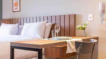 A hotel room with a bed, bedside table, chair, and an air conditioning unit.