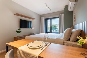 Una habitación de hotel con una cama, un televisor montado en la pared, una mesa de comedor con platos y cubiertos, y una ventana con cortinas.