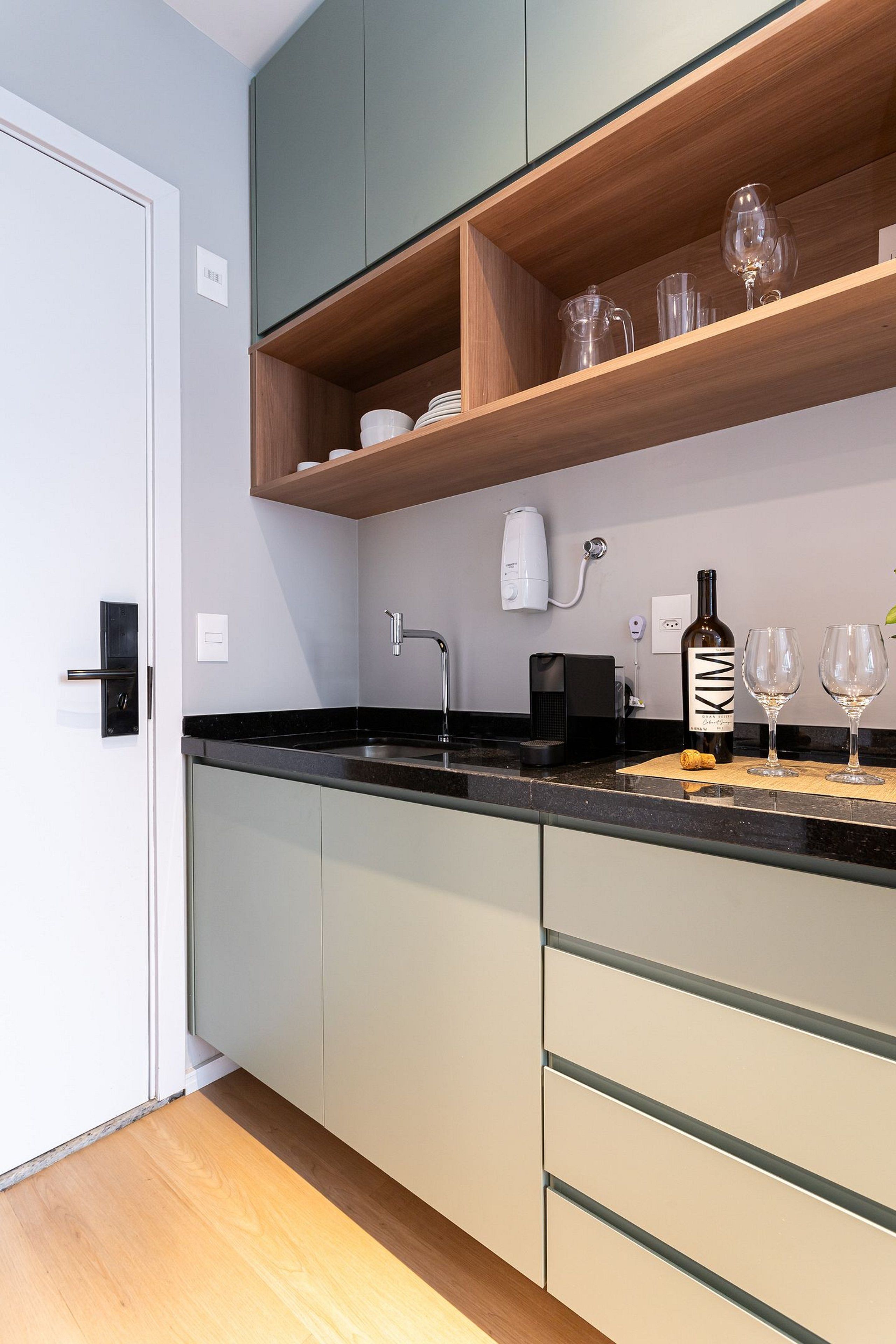 A modern kitchen with a black countertop, wooden shelves, and a wine bottle.