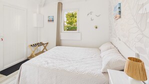 Una stanza bianca con un letto, una finestra vista sul verde, una porta e una parete con motivo a foglia.