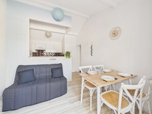 A modern living room with a sofa, dining table, chairs, and a kitchen in the background. - House for 4 people, 400m from the beach (Pornic)