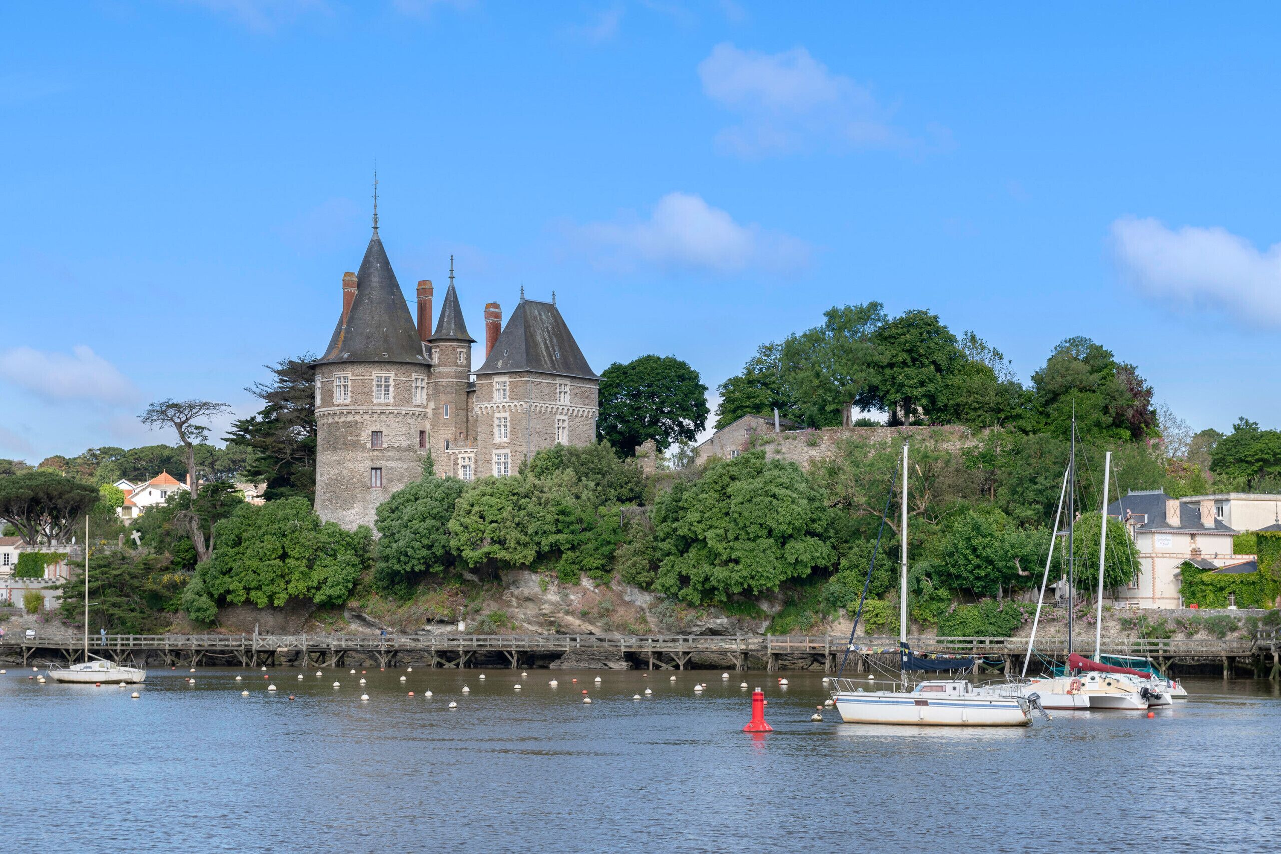 Un château historique, doté d’un fossé, entouré d’une végétation luxuriante et bordé d’une rivière paisible.