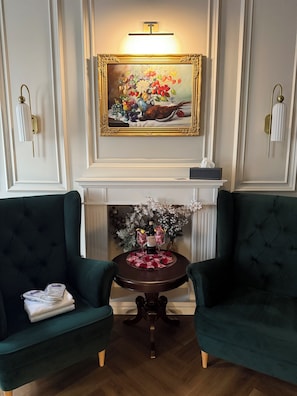 A room with a fireplace, two green armchairs, a small table with a bottle and glasses, and a framed painting above the mantel. - Apartament z Jacuzzi Kraków ART Koletek (Kraków)