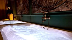 Una bañera con una superficie de agua amplia y transparente, un grifo de pared y un revestimiento decorativo con diseño de árbol.