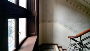 Una escalera con barandilla, un muro con diseño y un ventanal con balcón de metal.