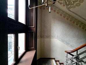 A staircase with a handrail, a patterned wall, and a window with a metal balcony. - Apartament z Jacuzzi Kraków ART Koletek (Kraków)