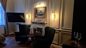 Una habitación con una televisión de pantalla plana, dos sillones, una mesita con un florero y una chimenea con un cuadro encima.