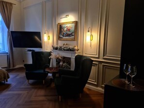 A room with a flat-screen TV, two armchairs, a small table with a vase, and a fireplace with a painting above it. - Apartament z Jacuzzi Kraków ART Koletek (Kraków)