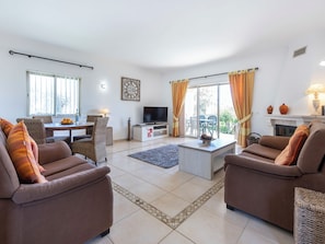 Ein Wohnzimmer mit zwei Sofas, einem Fernseher, einem Esstisch mit Stühlen und einem Kamin.