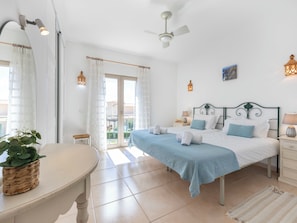 Ein Schlafzimmer mit Bett, Nachttischen, Deckenventilator, einem Fenster mit Vorhängen und Blick ins Freie.