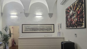 A reception area with a white reception desk, a framed cityscape artwork, a large abstract painting, and a potted plant. - Casa per Ferie degli Angiolini (Florence)