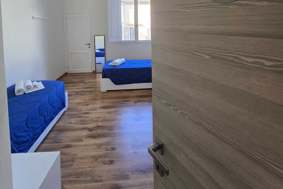 Une chambre avec deux lits, une porte en bois portant un numéro et une fenêtre.