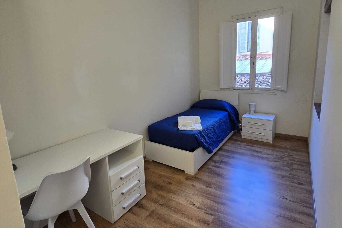 Une chambre à coucher avec un lit, un bureau, une chaise, une table de chevet et une fenêtre.