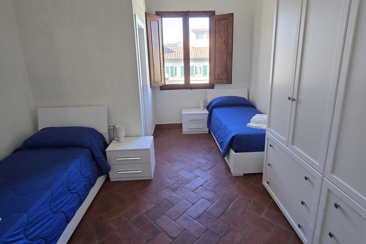 Une chambre avec deux lits, une armoire, une fenêtre avec des volets et un sol carrelé.