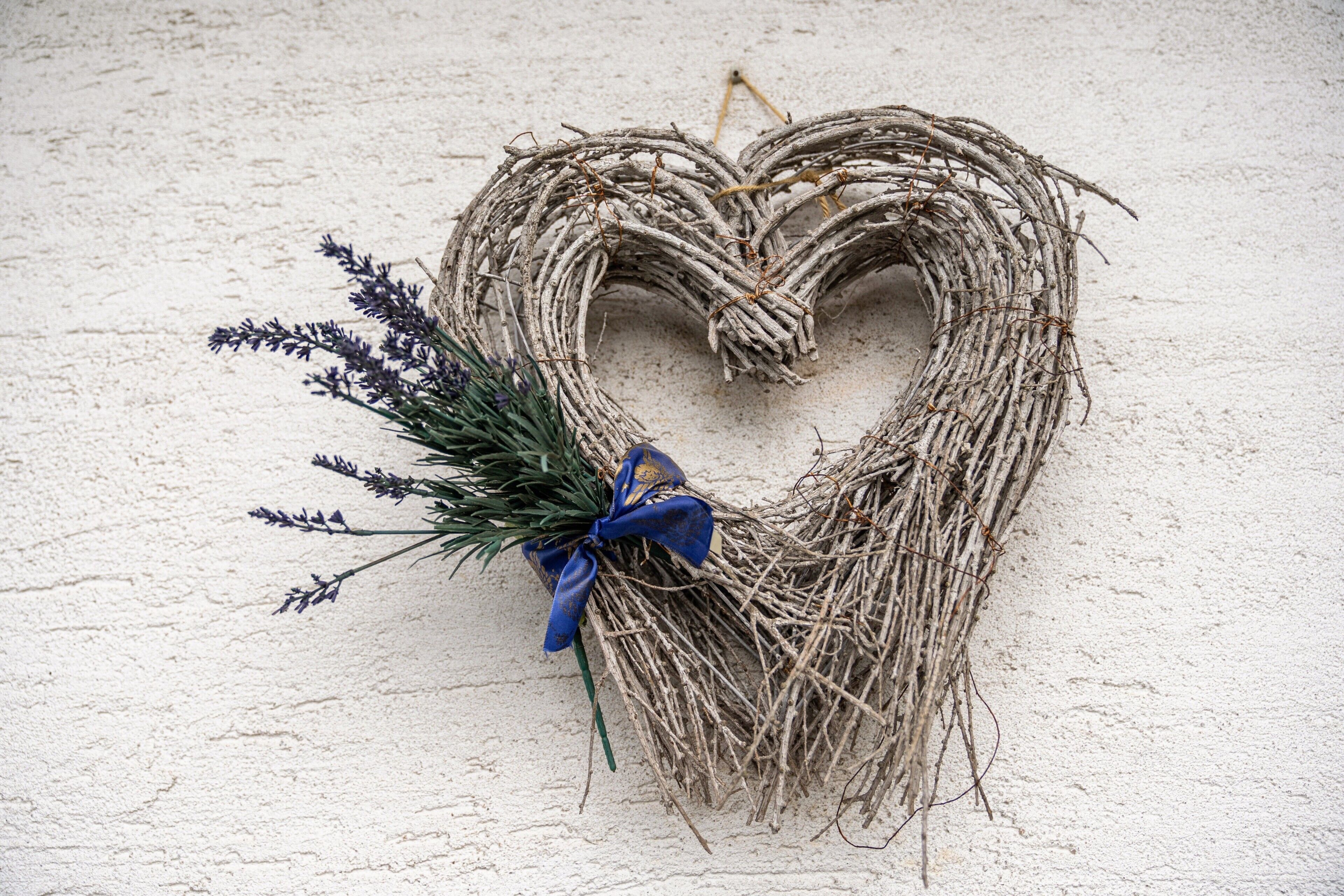 Ein herzförmiger Kranz mit blauem Band und Lavendel auf einer strukturierten Wand.