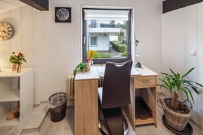 Ein Zimmer mit Holztisch, einem Stuhl, einem Blumentopf, einer Uhr und einem Fenster mit Blick auf ein Gebäude.