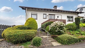 Een tweelaags huis met een witte gevel, een bruin dak en een kleine veranda met treden naar de ingang.