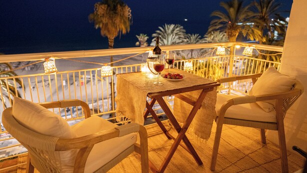 Ein Balkon mit Tisch und Stühlen für zwei Personen, einer Weinflasche und einem Weinglas.