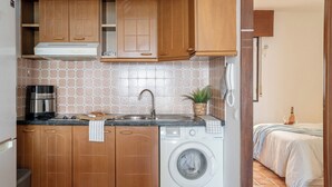 Eine kompakte Küche mit Holzausstattung, einer Kaffeemaschine, einer Waschmaschine und einer gefliesten Spritzschutzwand.