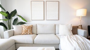 Ein Wohnzimmer mit einer Couch, einem Couchtisch mit Buch und Tasse, einer Lampe und einer großen Pflanze.