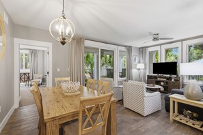 A spacious living area with a dining table, chairs, a sofa, a TV, and a ceiling fan. - RARE! Corner Unit Connected to Baytowne Wharf! Trop Pool, Hot Tub, Beach Tram (Miramar Beach)