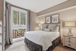 A bedroom with a large bed, a nightstand, a window with curtains, and a view of trees. - RARE! Corner Unit Connected to Baytowne Wharf! Trop Pool, Hot Tub, Beach Tram (Miramar Beach)