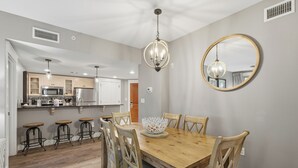 Un comedor con una mesa de madera, sillas, una araña y un espejo en la pared.