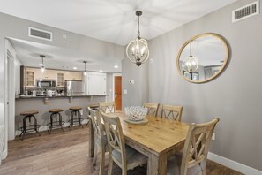 A dining area with a wooden table, chairs, a chandelier, and a mirror on the wall. - RARE! Corner Unit Connected to Baytowne Wharf! Trop Pool, Hot Tub, Beach Tram (Miramar Beach)