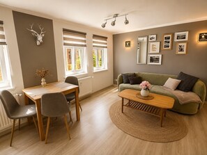 A modern living room with a dining area, a sofa, a coffee table, and a wall-mounted deer head decoration. - Blankenburg Harz Apartment, WANDERLUST (3 people), Old Town, Wi-Fi, garden, parking (Blankenburg (Harz))