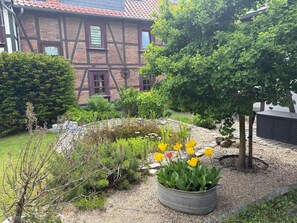 Ein Garten mit Teich, gelben Blumen und einem Gebäude mit Ziegeldach.