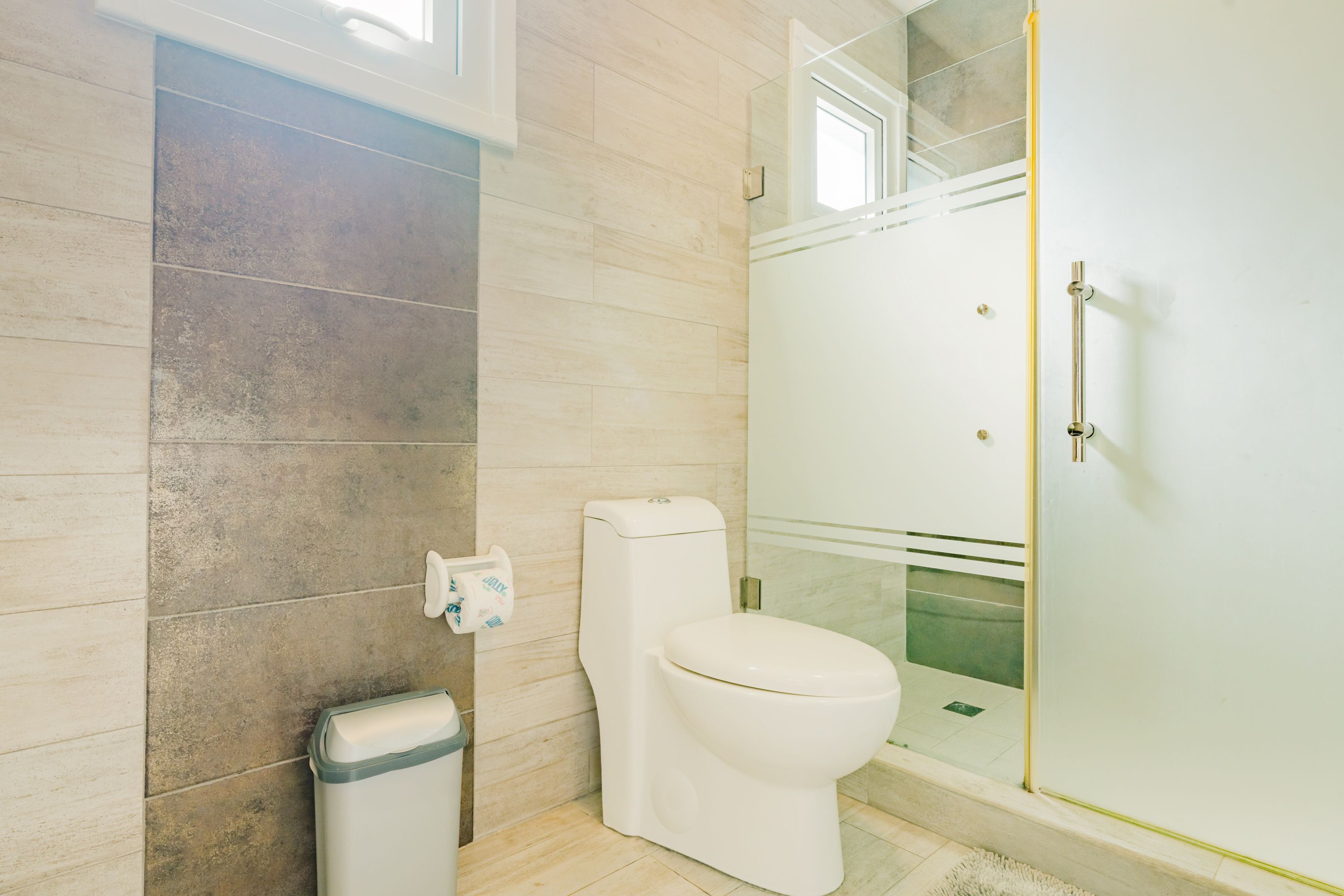 Bagno con toilette, cestino e zona doccia.
