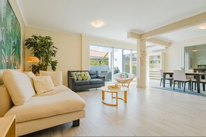 Ein modernes Wohnzimmer mit einer Couch, einem Esstisch mit Stühlen, einem Couchtisch und einer großen Topfpflanze.