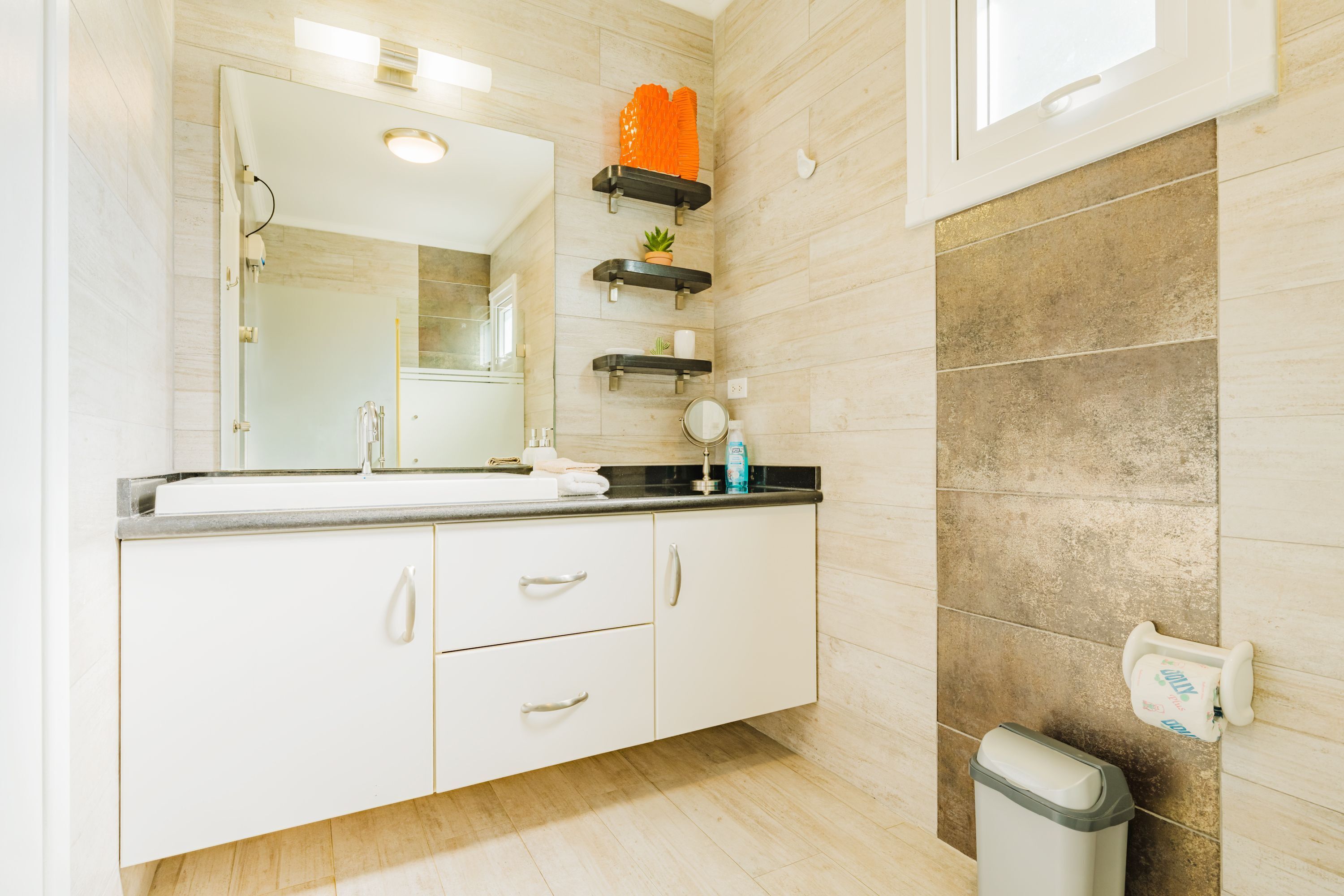 A bathroom with a white vanity, a mirror, a sink, and a trash bin.