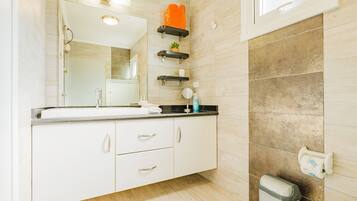 A bathroom with a white vanity, a mirror, a sink, and a trash bin.